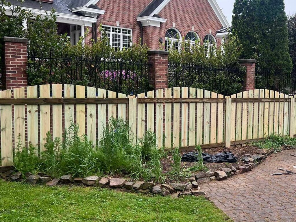 A charming scalloped wood fence installed in front of a brick residential home by RUCO Fence in Huntsville, AL.
