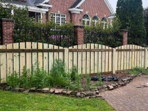 A charming scalloped wood fence installed in front of a brick residential home by RUCO Fence in Huntsville, AL.