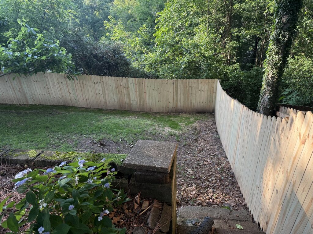 A newly installed scalloped wood fence on a sloped backyard property by Premier Fence of Birmingham, LLC in Warrior, AL.
