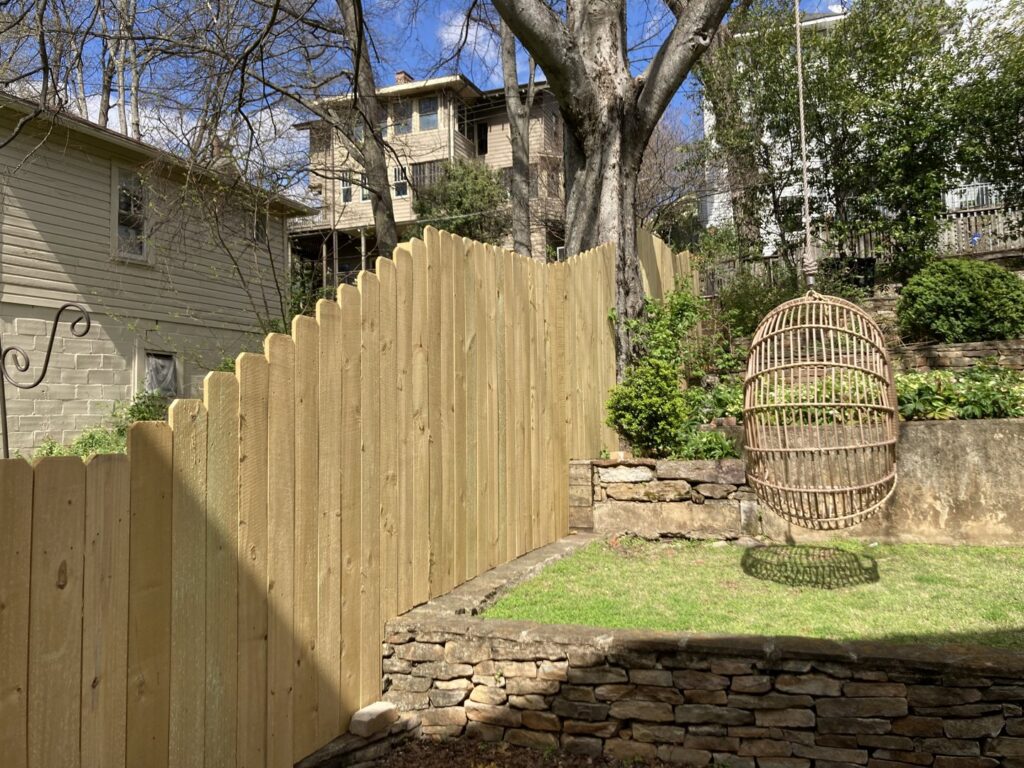 A newly installed scalloped wood picket fence on a sloped residential property by Premier Fence of Birmingham, LLC in Warrior, AL.