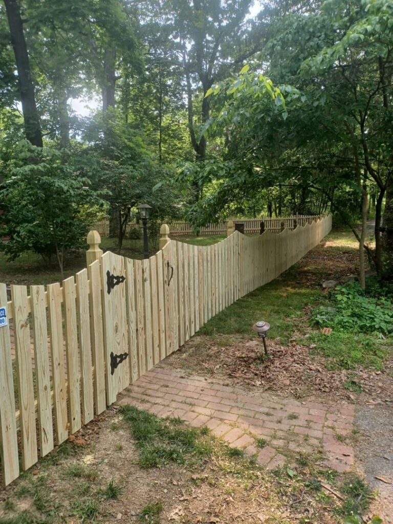 A charming scalloped wooden picket fence with a gate leading into a wooded area, installed by A Freedom Fence in Martinsburg, WV.