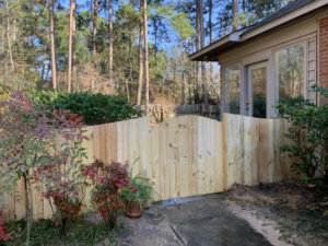 A scalloped natural wood privacy fence gate installed by Brock Brothers Fence next to a home in Mobile, AL.