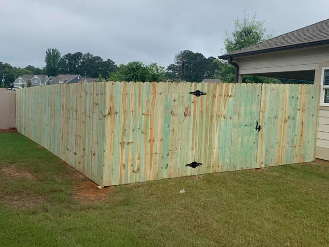 A scalloped wooden privacy fence with a gate providing security and style by Integrity Construction and Fencing, LLC in Clanton, AL.