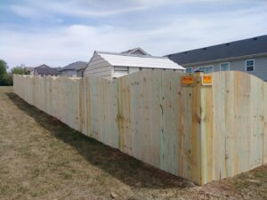 A long, newly installed scalloped wooden privacy fence with Roark Fencing signs, showcasing quality work in Lexington, KY.