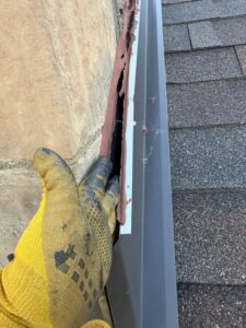 A gloved hand inspecting or sealing a gap along a roofline for wildlife exclusion by Prairie Bat Services, LLC in Sioux Falls, SD.