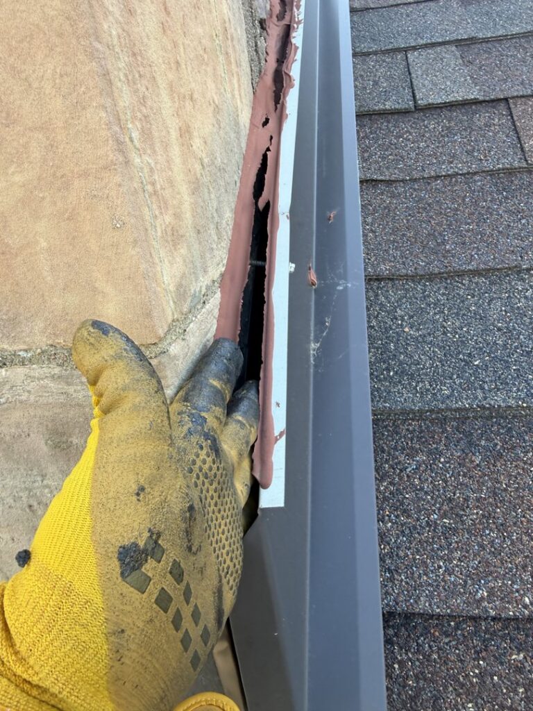 A gloved hand inspecting or sealing a gap along a roofline for wildlife exclusion by Prairie Bat Services, LLC in Sioux Falls, SD.