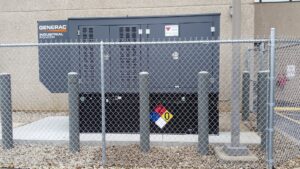 A Generac industrial power generator installation secured with a chain-link fence and bollards by Varitech, Inc. in Louisville, KY.