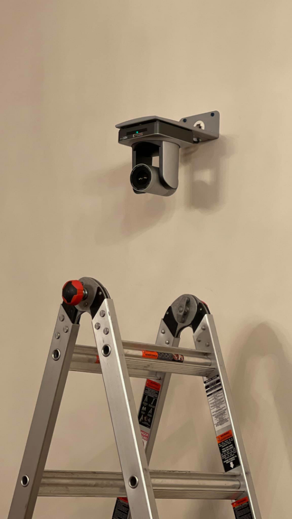 A security camera mounted on a wall with a ladder, indicating installation work by Gksquad in Columbia, SC.