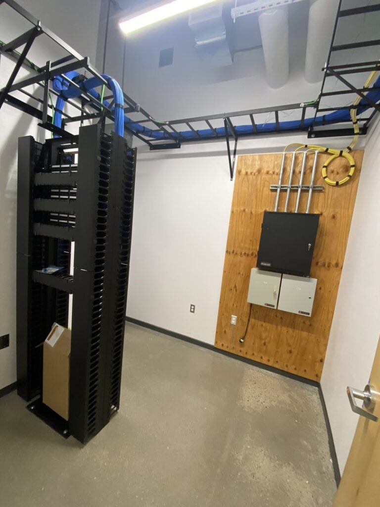 A server rack with structured data cabling and electrical panels installed on the wall by CAAM Integration LLC in Albuquerque, NM.