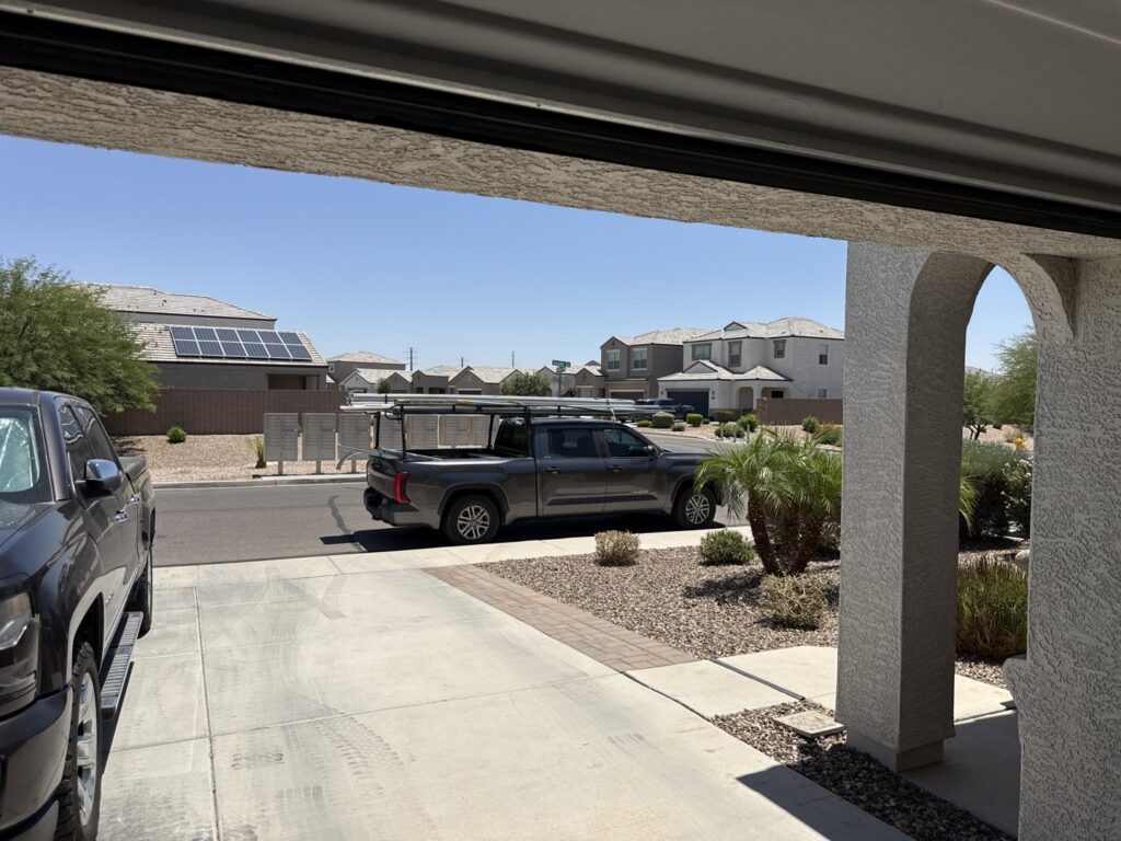 A service truck with a ladder rack parked outside a garage, indicating a job site for MGG Garage Door Service in San Tan Valley, AZ