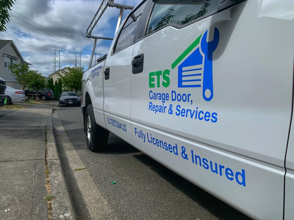 A white service truck for ETS - Garage Door & Electric Gate Repair Of Bellevue, WA, parked on a residential street.