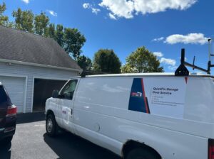 A QuickFix Garage Door Service van parked at a residential property with an open garage door, indicating a service call in Brighton, MA.