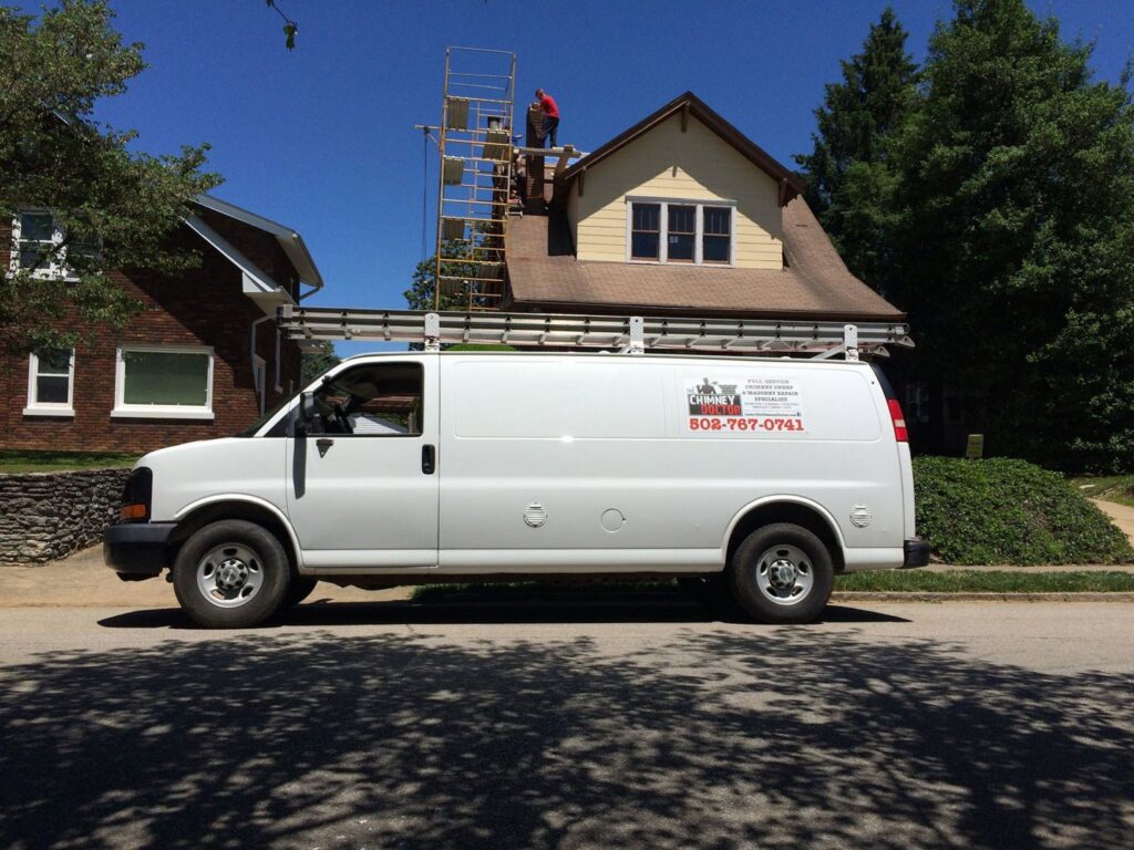 A service van from The Chimney Doctor parked on a street with workers on scaffolding repairing a chimney in Louisville, KY.