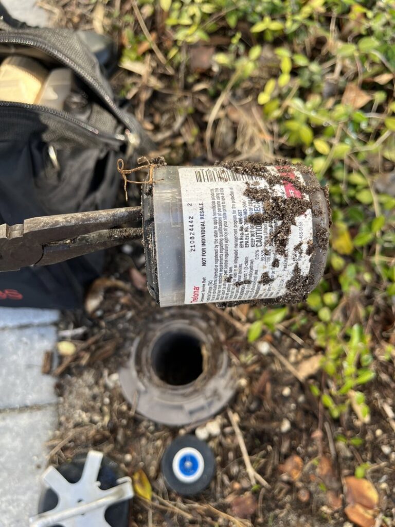 A pest control technician servicing an in-ground bait station for Crawford Pest Control in Jacksonville, FL.