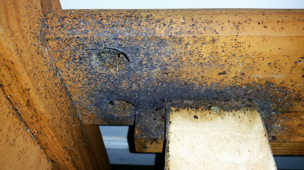 Severe bed bug infestation with numerous fecal stains and shed skins on a wooden bed frame, a job for Himalaya Pest Control in Alpharetta, GA.