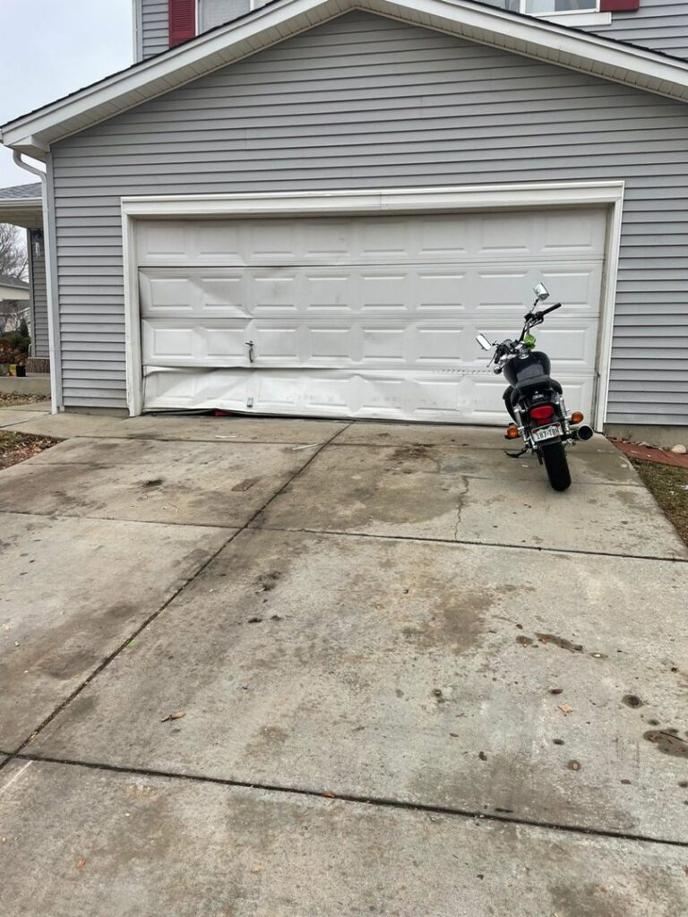 A severely damaged garage door with multiple bent panels, requiring repair or replacement from Greeley garage door repair in Greeley, CO.