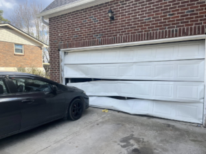 A severely damaged white garage door on a brick home, indicating a need for replacement from J&S Garage Door Services in Franklin, TN.