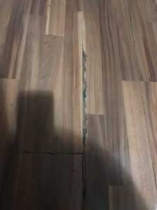 Severely damaged wood flooring with a large gap, indicating a need for replacement by Carpet and Flooring Liquidators - Dallas in Arlington, TX.