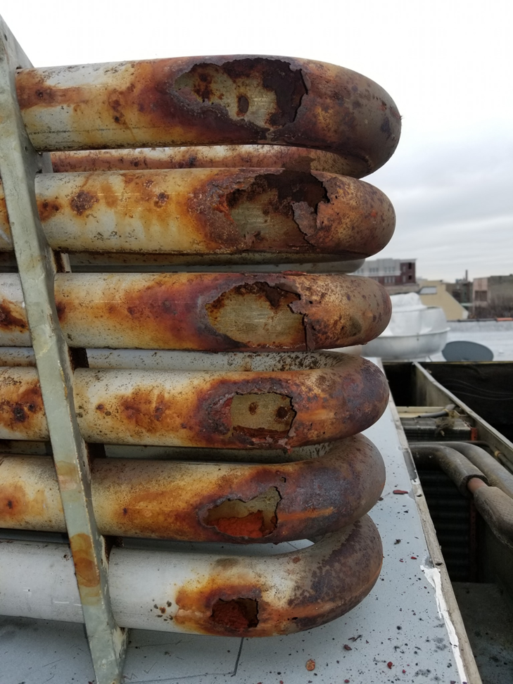 Close-up of severely rusted and damaged HVAC coils on a commercial unit, indicating needed repair by ARC Mechanical Inc in South Elgin, IL.