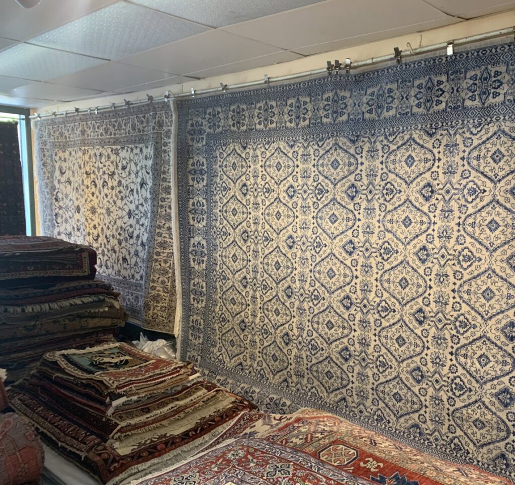 A showroom display featuring numerous hanging and stacked rugs at Danvers Rug in Danvers, MA.