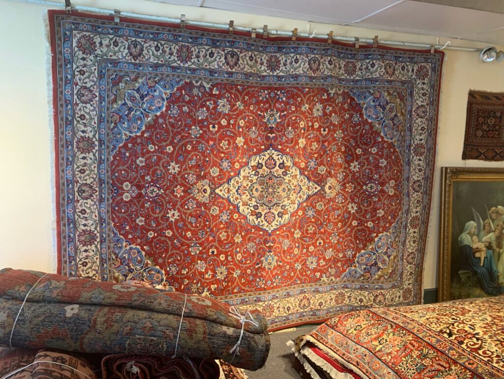 A showroom display featuring a large red ornate rug hanging on a wall at Danvers Rug in Danvers, MA.