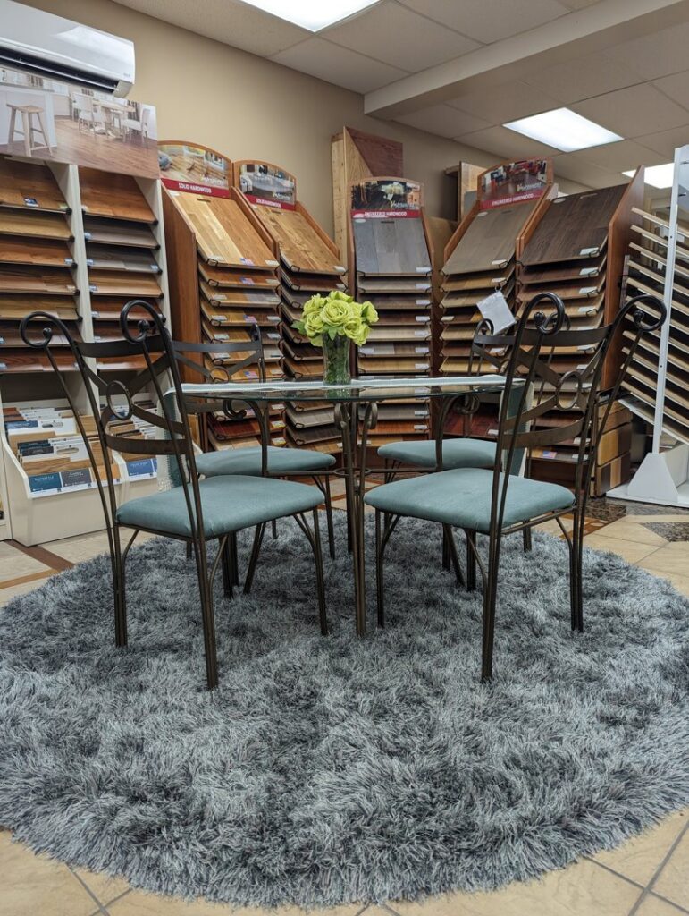 A showroom display featuring a plush round gray rug and various hardwood flooring samples at Petersen's Carpet & Flooring in Frederick, MD