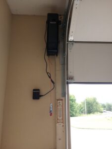 A side-mount garage door opener installed next to a white garage door by Precision Garage Door of Owensboro Evansville in Owensboro, KY.