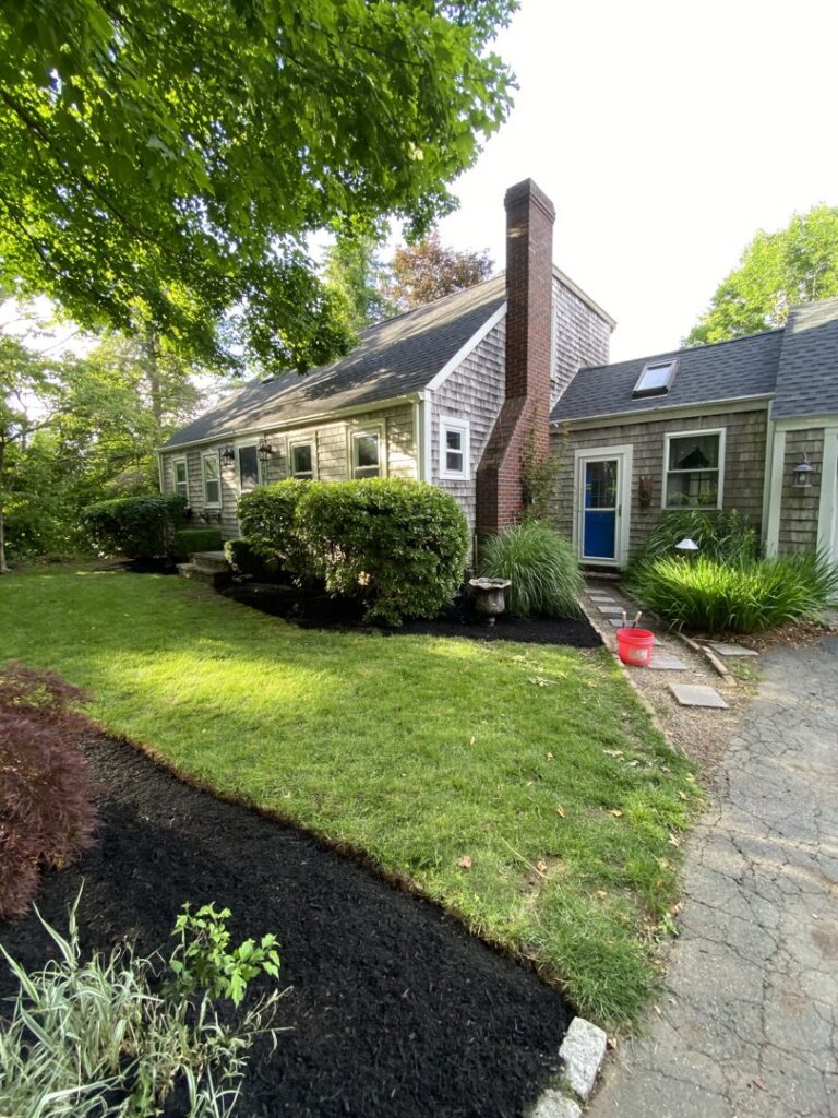 A neatly landscaped side yard with fresh mulch beds and a green lawn by Chaves Lawn Care in New Bedford, MA