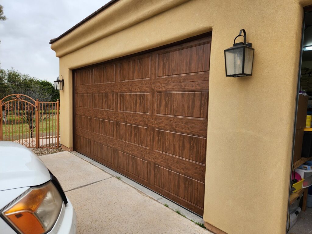A single brown garage door with a wood grain finish installed on a stucco home by JT's Overhead Doors in Gilbert, AZ.