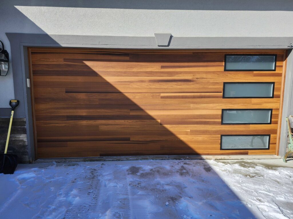 A single modern wooden garage door with vertical windows, showcasing an installation by Steve's Overhead Door Company in Lafayette, IN.