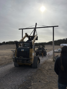 A skid steer lifting a large metal gate frame for installation by Cool Hand Fencing and Wyo War Wagons in Laramie, WY.