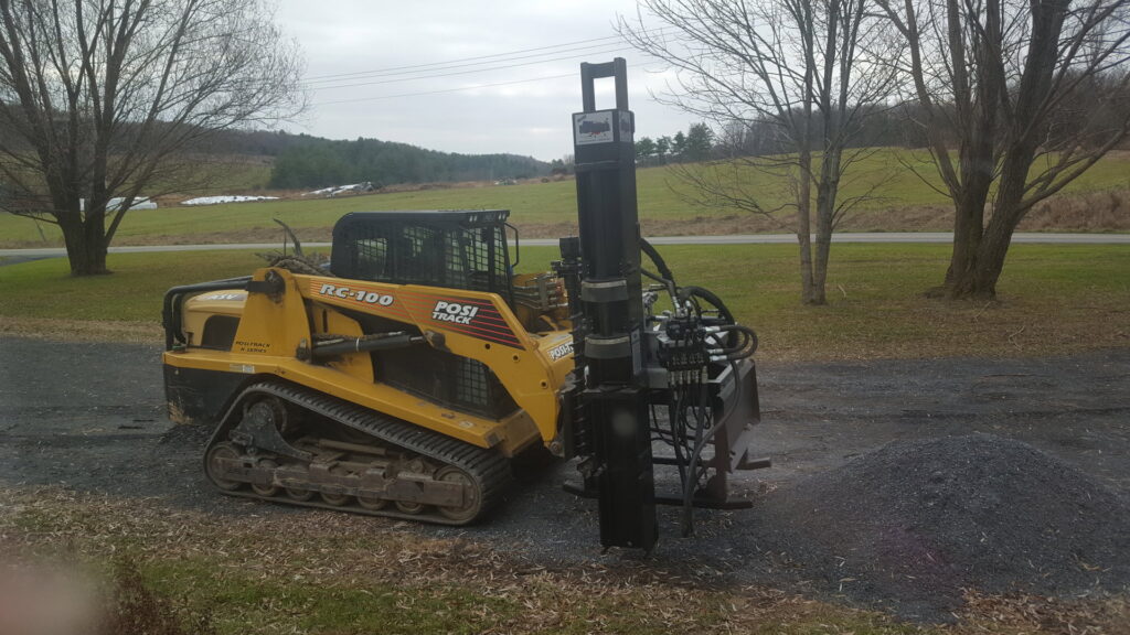 A skid steer with a post driver attachment, equipment used by 802 Fence Company LLC for fencing jobs in Shoreham, VT.