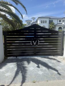 A sleek black horizontal slat gate with a custom 'V' emblem, installed by A Master Work Corp. in Hialeah, FL.
