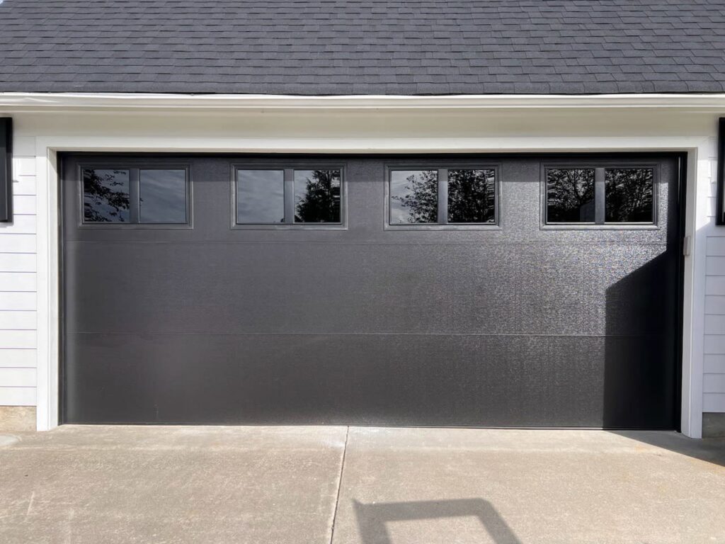 A sleek black modern garage door with horizontal windows, expertly installed by Rainier Garage Door in Bellevue, WA.