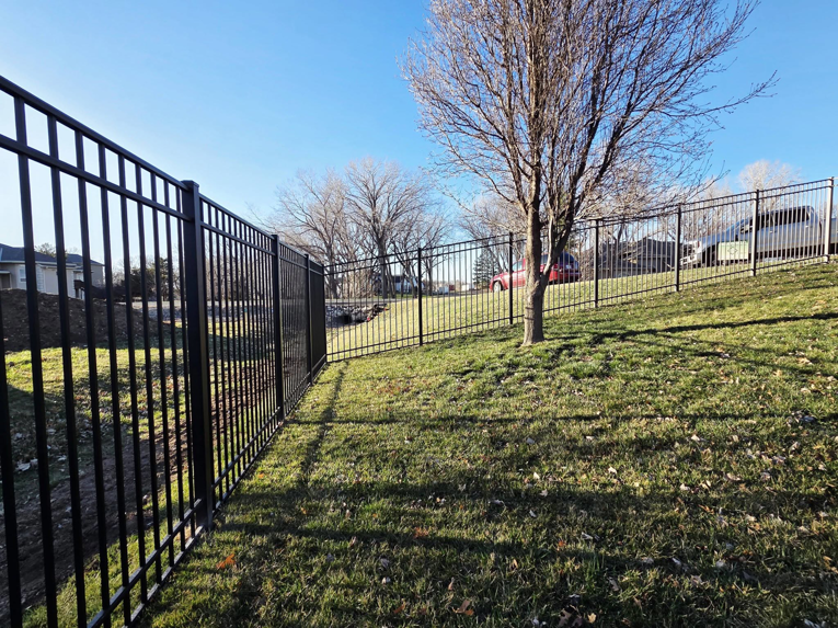 A long stretch of black metal fence installed on a sloped residential property by Green Acres Fence Co in Salina, KS.