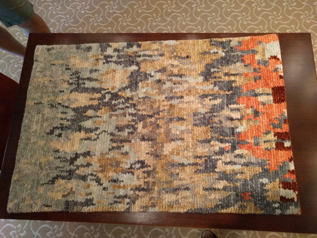 A small abstract patterned rug displayed on a wooden table, showcasing a product from David Alan Rugs in Austin, TX.