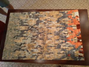 A small abstract patterned rug displayed on a wooden table, showcasing a product from David Alan Rugs in Austin, TX.