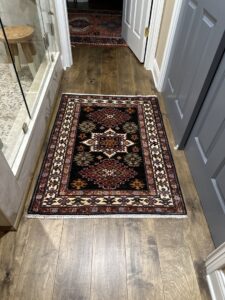 A small, dark patterned rug placed on a hardwood floor in a bathroom, provided by Yas Rugs in Lexington, KY.