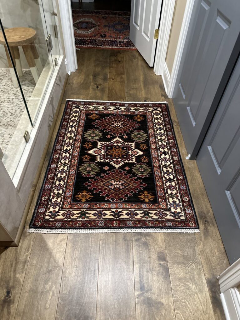 A small, dark patterned rug placed on a hardwood floor in a bathroom, provided by Yas Rugs in Lexington, KY.