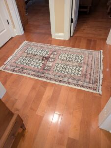 A small, intricately patterned runner rug in pink and white on a hardwood hallway floor, from Yas Rugs in Lexington, KY.
