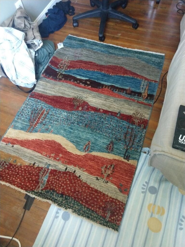 A small, colorful tribal rug with a landscape design placed on a wooden floor by Yayla Tribal Rugs, Inc. in Cambridge, MA.