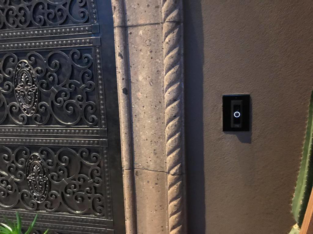 A smart doorbell installed on a wall next to an ornate gate by Lundell Electrical Services in Mesa, AZ.