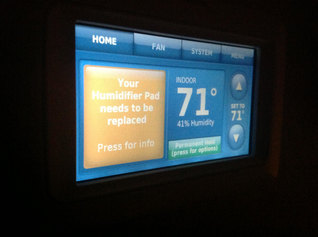 A smart thermostat displaying a message for humidifier pad replacement, serviced by Cool Fish Refrigeration, Heating, and Air in Minot, ND.