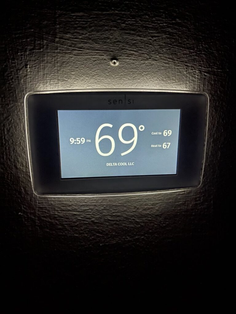 A smart thermostat displaying "Delta Cool LLC" and current temperature settings, showcasing a professional installation by DeltaCool in Jonesboro, AR.