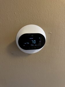 A modern smart thermostat installed on a wall, showing temperature settings, by OnPoint Heating and Air in Commerce City, CO.