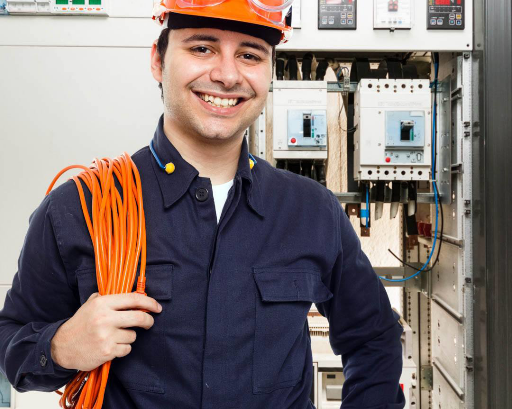 A smiling electrician from Lewis Electric holding electrical cable in front of a service panel in Macon, GA