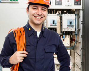A smiling electrician from Lewis Electric holding electrical cable in front of a service panel in Macon, GA
