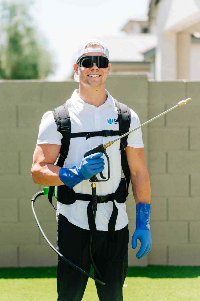 A smiling pest control technician from Aloe Pest Control wearing a backpack sprayer in Mesa, AZ.