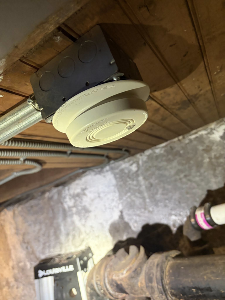 Connecting a smoke detector to an electrical box on a wooden ceiling by Dartmouth Fire Protection Electrical Division in New Bedford, MA.
