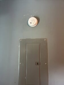A smoke detector installed above an electrical panel by Mister Sparky Kansas City, MO.